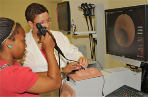 A high school student manipulates a scope inserted into the nasal passages of a simulated human head.