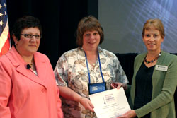 Ms. Louise Van Diepen (right), Deputy Chief Learning Officer, and Dr. Paula Molloy (left), SimLEARN National Program Manager, present LeAnn Schlamb (center) with an award for Best in Show.